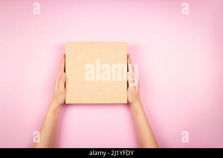 Top view to female hands holding brown cardboard box on pastel pink background. Mockup parcel box. Packaging, shopping, delivery concept Stock Photo