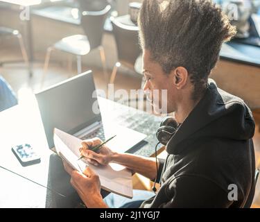 young afro american man studying with laptop, taking notes on notebook, young latin american prepares for a university exam using modern technological Stock Photo