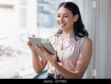 Technology eases the work load. Shot of an attractive young businesswoman standing alone in the office and using a digital tablet. Stock Photo