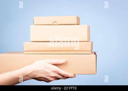 Stack of cardboard boxes in female hands. Blank brown parcel boxes on light blue background. Packaging, shopping, free shipping, delivery concept Stock Photo