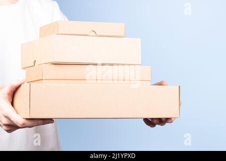 Stack of cardboard boxes in female hands. Blank brown parcel boxes on light blue background. Packaging, shopping, free shipping, delivery concept Stock Photo