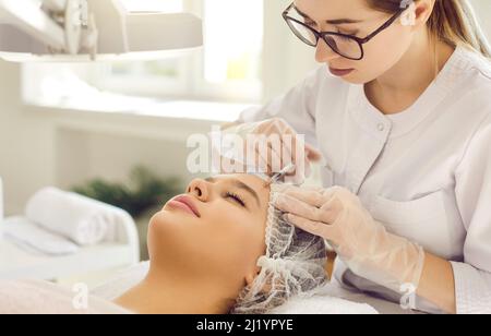 Woman is getting aesthetic treatment and receiving injection in her forehead Stock Photo