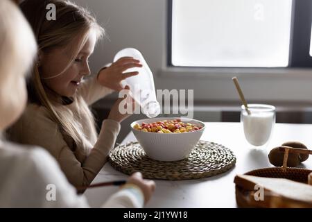 Cute caucasian siblings sitting at table on kitchen early morning and preparing breakfast with colorful cornflakes and milk. Kids enjoying life with Stock Photo