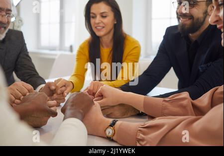 Team of happy supportive business people sitting around an office table and holding hands Stock Photo