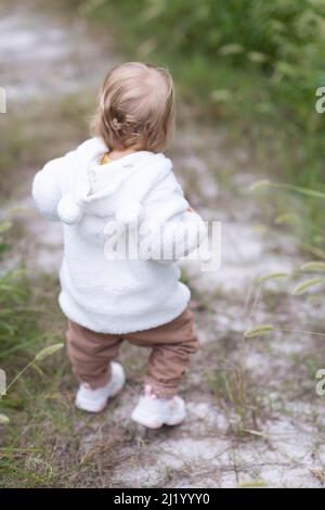 Portrait of cute little caucasian baby girl one year old takes the first steps and learns to walk in park at autumn. Stylish infant with blonde hair Stock Photo