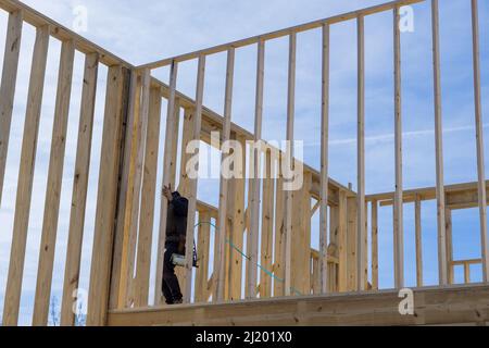 Worker in holding plank installing it on household construction using air hammer in nailing wooden beams Stock Photo