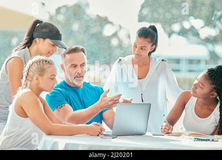 You learn more when you watch your performance. Shot of a handsome mature coach sitting and using a laptop while discussing a game plan with his Stock Photo