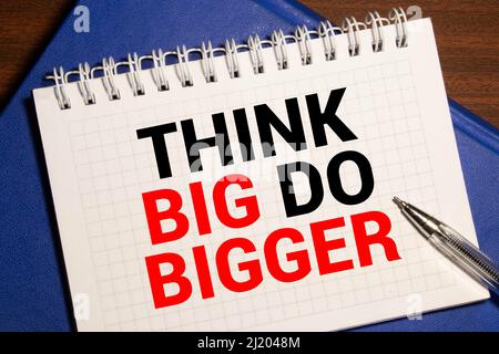 Think Big, Do Bigger Motivation quote notepad writing on dark background with pen Stock Photo