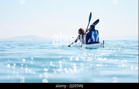 Exploring the scenic lakeside. Rearview shot of a young couple kayaking together at a lake. Stock Photo