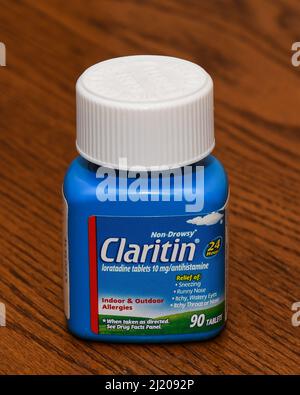 A blue bottle of 90 Claritin, loratadine tablets a non drowsy antihistamine for indoor and outdoor allergy relief isolated on an oak desk. Stock Photo