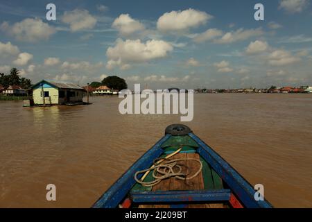 A boat is moving along river Musi, about to go past a floating house in Palembang, South Sumatra, Indonesia. In Srivijaya times, there were many citizens lived on floating houses along the river. I-Tsing (Yijing), a 7th century Chinese monk who travelled the maritime silk road to reach India to learn Buddhism, wrote on his notes that the sail from present day Guangzhou took 20 days, before 'the ship reached the capital of Srivijaya), where I landed and stayed six months, gradually learning the Sabdavidya (Sanskrit grammar).' Stock Photo