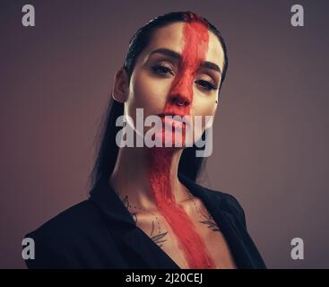 Your beauty puts me at ease. Studio shot of a young woman posing with paint on her face on a grey background. Stock Photo