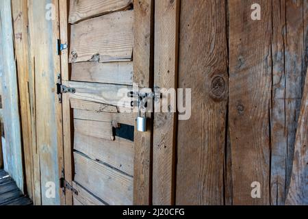 Angled view of a rustic, wooden door with a metal latch and padlock keeping it secure Stock Photo