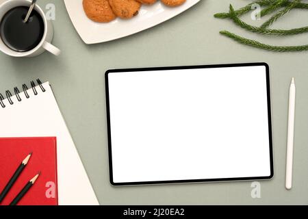 Modern office desk with digital tablet white screen mockup, spiral notepad, stationery, stylus pen, a cup of coffee, croissant and decor on green back Stock Photo