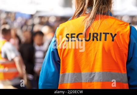 Safety is the main aim. Rearview shot of a security officer standing outdoors with a crowd in the background. Stock Photo
