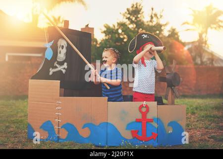 These little pirates just want to have fun. Shot of a cute little boy and his brother playing pirates outside on a boat made of cardboard boxes. Stock Photo