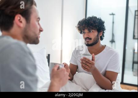 Cute man drinking coffee with his partner in the bedroom Stock Photo