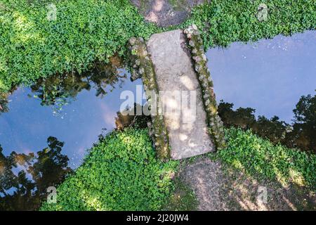 small stone footbridge over calm stream. water with reflections of sky and trees. aerial photo. Stock Photo