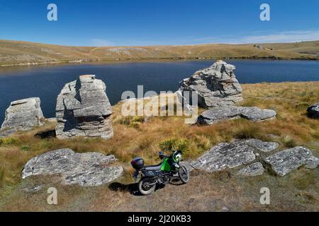 Adventure motorcycle by Logan Burn Reservoir (aka Great Moss Swamp), by Old Dunstan Trail, Central Otago, South Island, New Zealand - drone aerial Stock Photo
