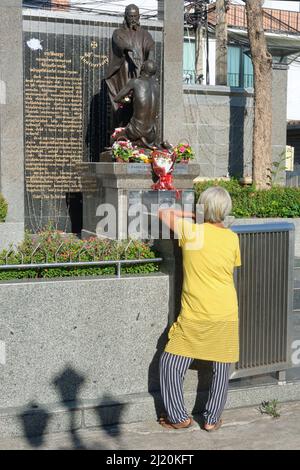 Outside St. Francis Xavier Church in Ban Yuan, Samsen, Bangkok, Thailand, a woman stands in front of a statue of Jesus healing the blind Bartimaeus Stock Photo