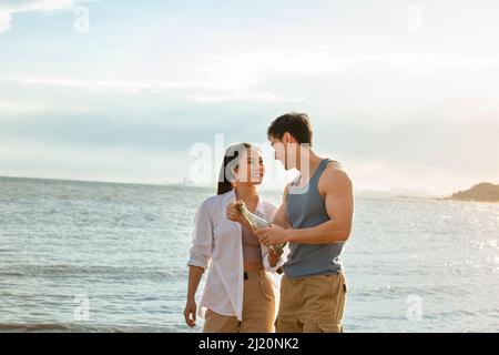 Young couple filling message in drift bottle on summer beach - stock photo Stock Photo