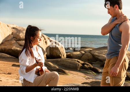 Young couple enjoying and playing ukulele on the beach rock - stock photo Stock Photo