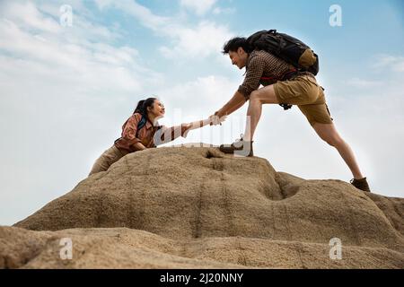 Mountaineers reaching out to help each other on steep rocky peaks, low angle view - stock photo Stock Photo