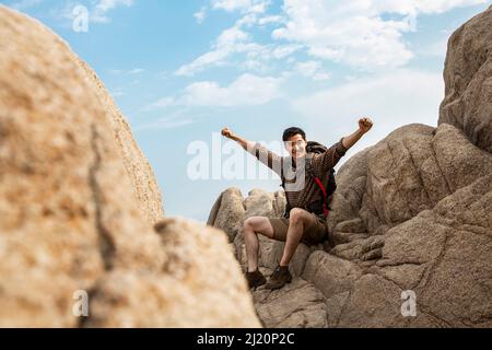 Cheering young backpacker with outstretched arms on rocky peaks - stock photo Stock Photo