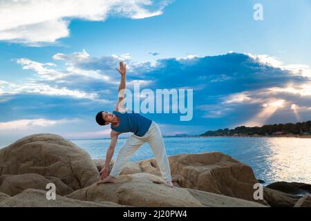 Muscular young man doing yoga on a beach rock - stock photo Stock Photo