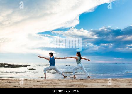 Young couple practicing yoga stretches on the beach - stock photo Stock Photo