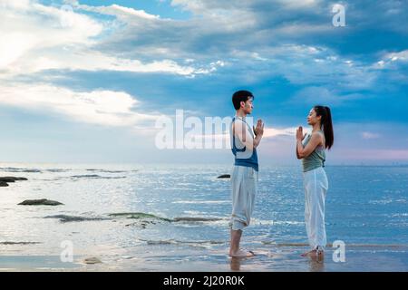 Young couple practicing yoga meditation while standing on the beach - stock photo Stock Photo