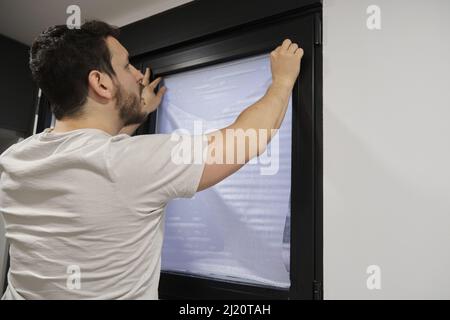 Man installing frosted window vinyl on wet window glass. Stock Photo