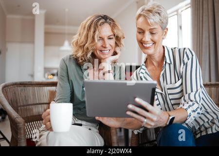 We have to watch these videos. Shot of two female friends drinking coffee while using a digital tablet. Stock Photo