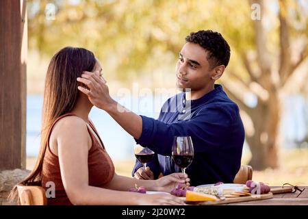 Sitting next to her is always the best seat in the house. Shot of a young couple having wine on a date on a wine farm. Stock Photo