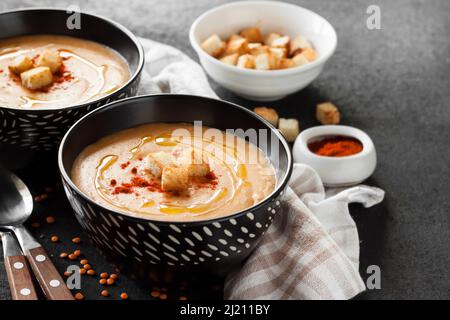 Lentil cream soup with paprika and crouton in black ceramic bowls on dark background Stock Photo