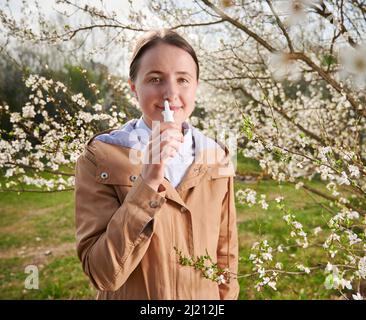 Woman allergic suffering from seasonal allergy at spring, posing in blossoming garden at springtime, using nasal drops. Spring allergy concept Stock Photo