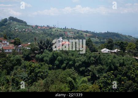 red and white roofs, visible in the hills, blocked by green trees, white clouds and a faded blue sky Stock Photo