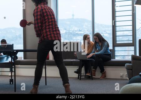 Two business women sitingt in a modern coworking space on a break from work and relax using a laptop. Selective focus  Stock Photo