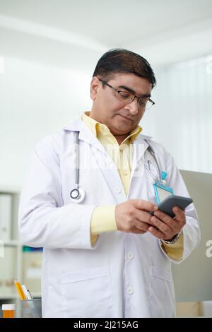 Serious mature Indian general practitioner reading text messages on smartph Stock Photo