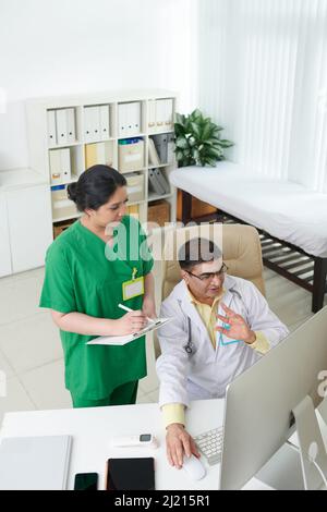 Diverse doctors discussing difficult medical case when looking at cardiogram or x-ray of patient on computer screen Stock Photo