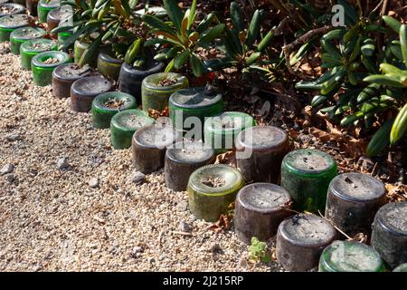 Creative reuse of old glass bottles as a border in the garden Stock Photo