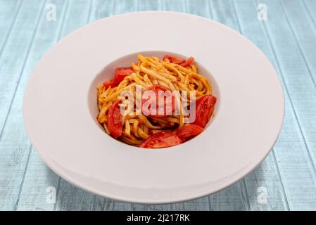 Italian Bavette pasta with tomato sauce, parmesan and fresh cherry tomatoes in white plate on light blue wood table Stock Photo