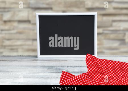 Food recipe template. Empty black board on a table with red checkered cloth against abstract blurred concrete wall. For your food product placement or Stock Photo