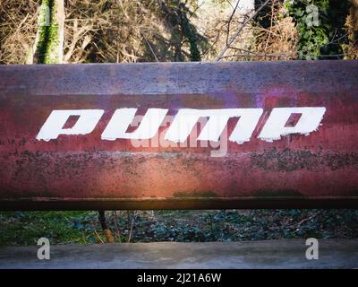 Rusty iron pipe with white text. Word PUMP written on a pipe. Stock Photo