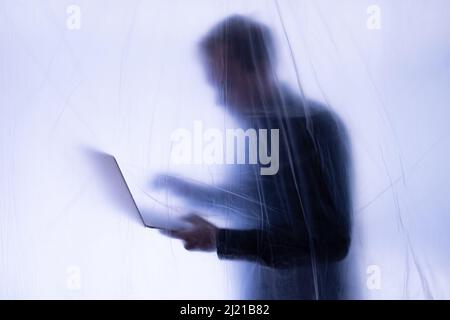 Anonymous Hacker commits cyber crime with laptop held in hand Stock Photo