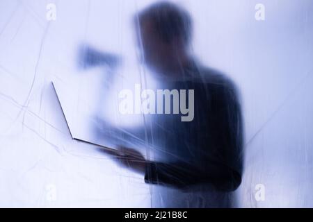 Anonymous Hacker commits cyber crime with notebook in hand. An axe is hold to symbolize forcefully intruding of IT systems for exploiting. Stock Photo