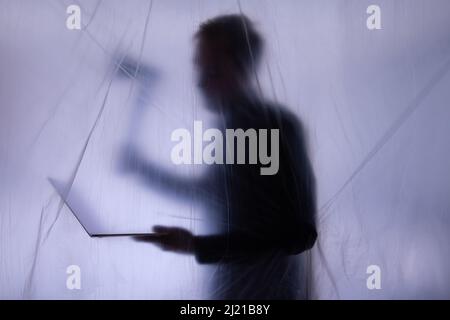 Anonymous Hacker commits cyber crime with notebook in hand. An axe is hold to symbolize forcefully intruding of IT systems for exploiting. Stock Photo