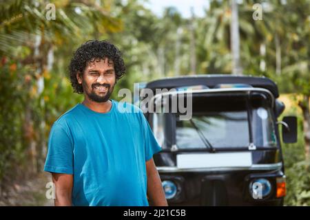 Portrait of smiling tuk tuk driver on rural road. Popular three wheeled motorcycle in Sri Lanka. Stock Photo