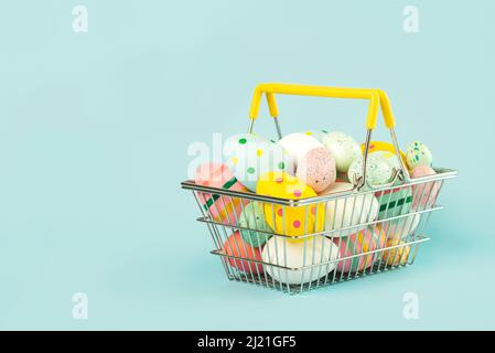 Happy Easter. Colored easter painted eggs in a shopping basket with copy space over blue background Stock Photo