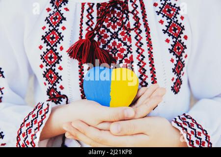 Small little girl in national traditional embroidery or embroidered shirt hold stone heart shape with Ukrane national flag. Love native country and people. Pray for Ukraine piece. High quality photo Stock Photo